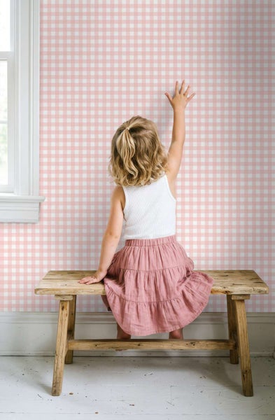Ein Kind sitzt auf einer rustikalen Holzbank vor einer Wand mit karierter Tapete in einem Kinderzimmer.