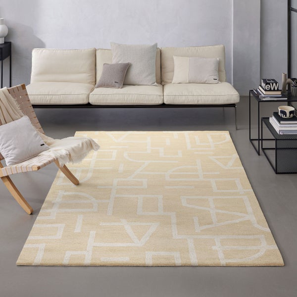 Modernes, helles Wohnzimmer mit geometrisch gemustertem Teppich, Textilsofa, Holzstuhl mit Flechtwerk und Beistelltischen aus Metall.