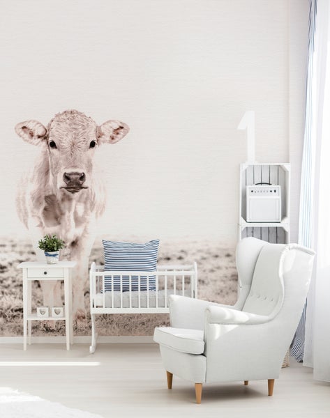 Modernes Zimmer mit Fototapete einer Kuh, weißem Sessel, Babywiege aus Holz und einem Beistelltisch in hellem Design.