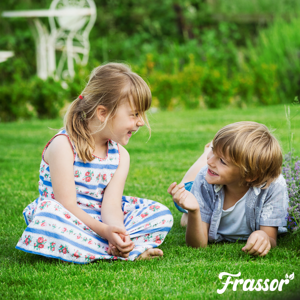 Zwei spielende Kinder auf einem dichten, gepflegten Rasen in einem hellen Garten. Frassor Logo.