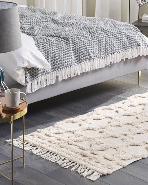 Modernes Schlafzimmer mit einer gemusterten Wohndecke mit Fransen auf dem Bett und einem hellen, strukturierten Teppich auf dunklem Boden.