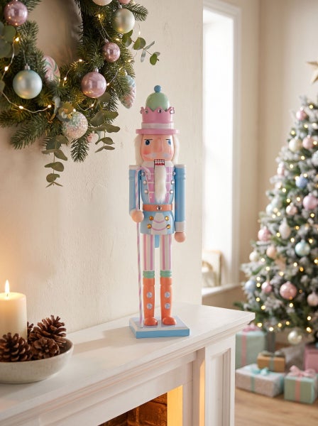 Dekorativer Nussknacker als Weihnachtsschmuck auf einem Kaminsims in einem festlich dekorierten Wohnzimmer mit Adventskranz und Weihnachtsbaum.