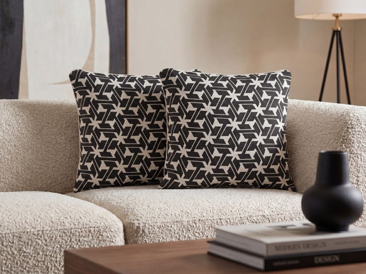 Zwei quadratische Dekokissen mit schwarz-weißem geometrischem Muster auf einem hellen strukturierten Sofa in einem modernen Wohnzimmer.