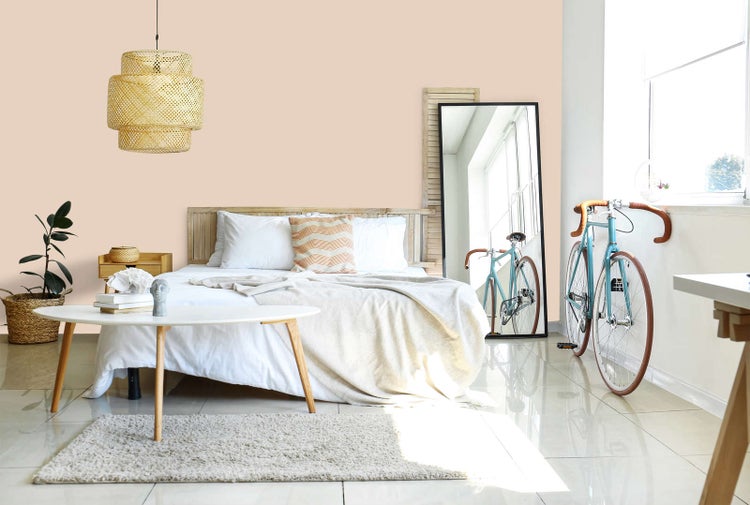 Modernes Schlafzimmer mit apricotfarbener Wand, Holzbett mit weißer Bettwäsche, geflochtener Pendelleuchte, großem Standspiegel und einem Fahrrad.