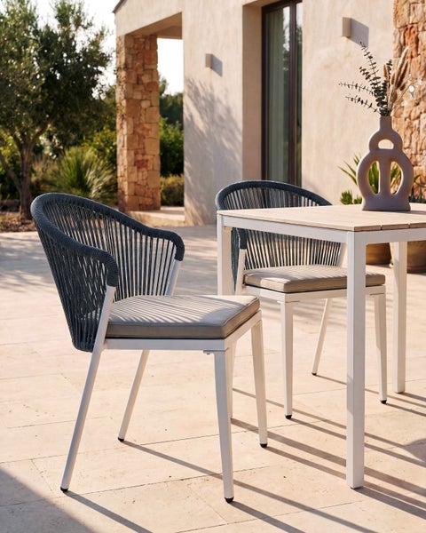Gartenstühle mit Geflechtbespannung und Sitzpolstern auf einer Terrasse mit Gartentisch und Vase.