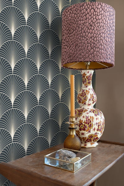 Dekoratives Interieur mit Tapete im Art-Déco-Stil, Tischlampe und Kerzenständer auf einem Holztisch.