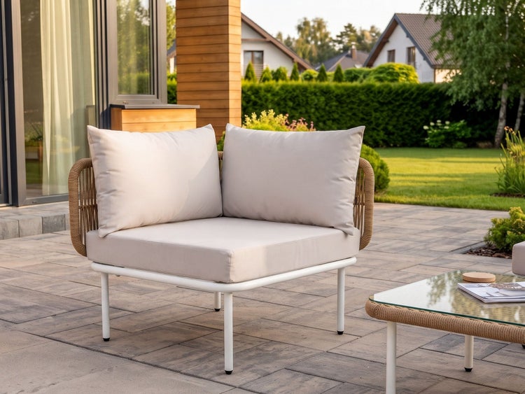 Moderner Garten-Ecksessel mit weißem Metallgestell, Seilgeflecht-Details und beigen Kissen auf einer gepflasterten Terrasse.
