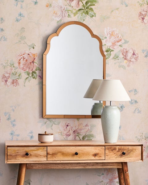 Dekoratives Interieur mit Spiegel, Lampe und Holzkonsole vor floraler Tapete