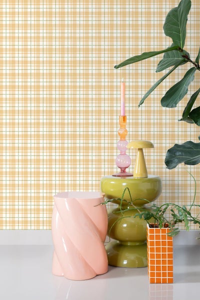 Innenaufnahme eines Raumes mit karierter Tapete und dekorativen Elementen wie einem Hocker, einer Blumensäule, einer Kerze und einer Zimmerpflanze