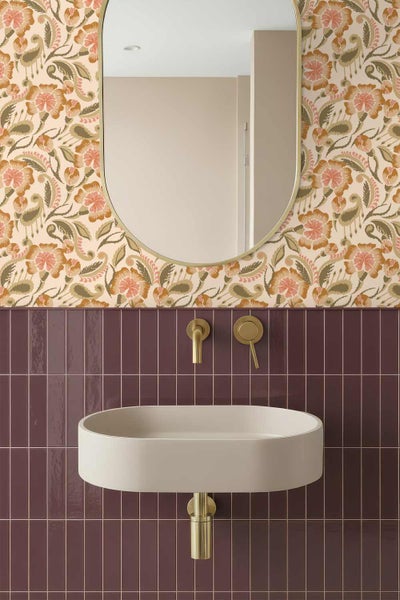 Modernes Badezimmer mit ovalem Wandwaschbecken, bordeauxroten vertikalen Fliesen, geblümter Tapete, ovalem Spiegel und goldfarbenen Armaturen.