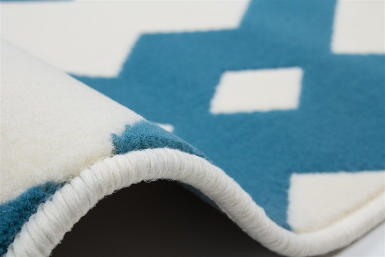 Blau-weißer Teppich mit geometrischem Muster, Detailaufnahme von Flor und geketteltem Rand.