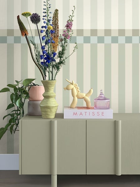 Dekoratives Arrangement auf einem Sideboard mit Blumen, Vase und Dekorationsfiguren vor einer gestreiften Wand