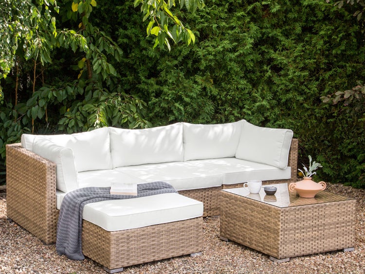 Gartenszene mit Rattansofa, Hocker und Tisch mit Accessoires im Freien