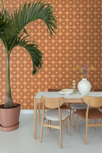 Ein Esszimmer mit retro-gemusterter Blumentapete, einem Esstisch aus Holz mit passenden Stühlen und einer großen Zimmerpalme.