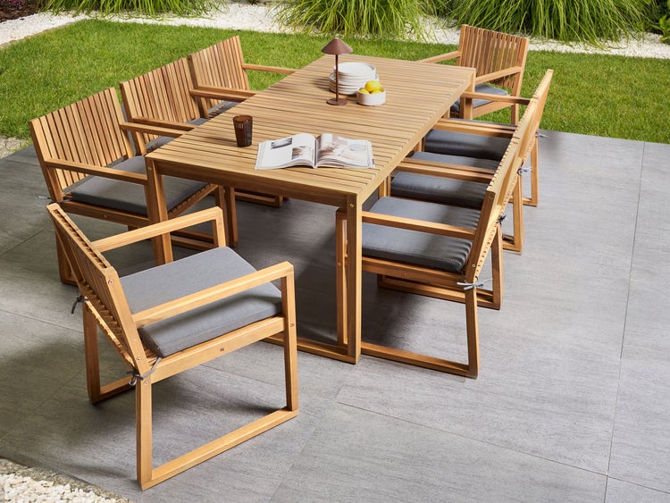 Gartenszene mit Holztisch und Stühlen mit Sitzkissen auf einer Terrasse