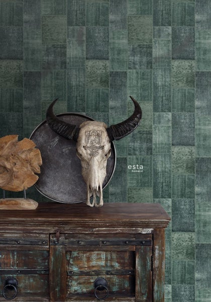 Dekoratives Arrangement mit Büffelschädel, Holzornament und Kommode vor Patchwork Tapete