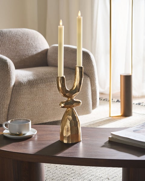 Dekorative Szene mit einem goldenen Kerzenständer auf einem Tisch, inklusive Kerzen, einer Tasse und einem Sessel