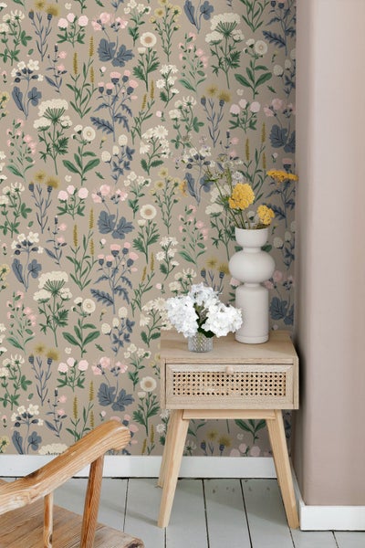 Vliestapete mit floralem Wiesenblumenmuster in einem hellen Zimmer mit einem Nachttisch aus Holz und Rattan sowie Vasen auf einem Holzboden.