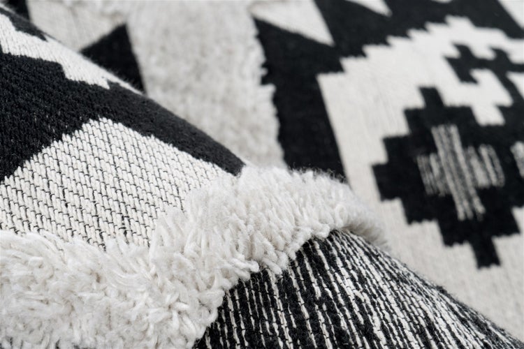 Detailaufnahme eines Teppichs mit schwarz-weißem geometrischem Muster und verschiedenen Texturen wie Flachgewebe und Hochflor.