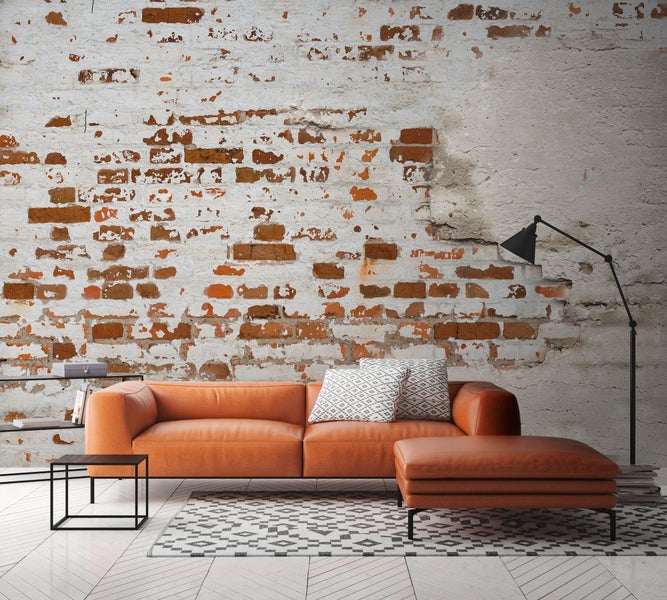 Wohnzimmer im Industriestil mit Leder-Sofa, passendem Hocker, gemustertem Teppich und einer Wand in Backsteinoptik.