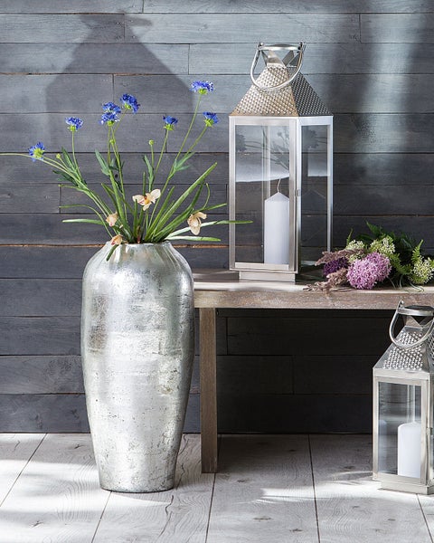 Dekorative Szene mit silberner Vase mit Blumen, Windlichtern und Blumensträußen auf einem Holztisch.