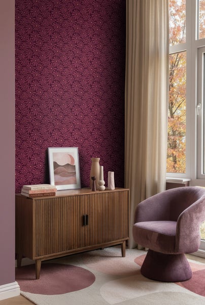 Vliestapete mit violettem Blumenmuster an einer Wand hinter einem Sideboard aus Holz und einem Sessel.