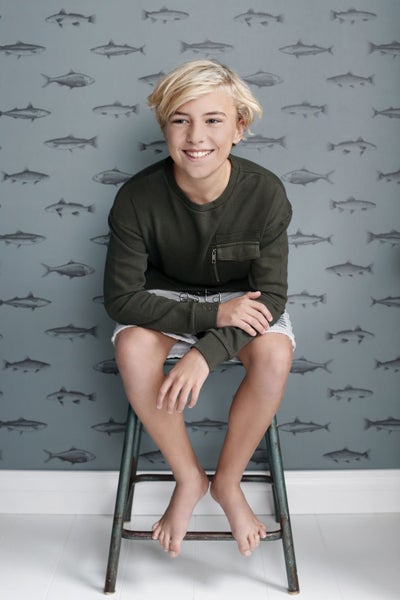 Ein Junge sitzt auf einem Hocker vor einer Wand mit Fischmuster.