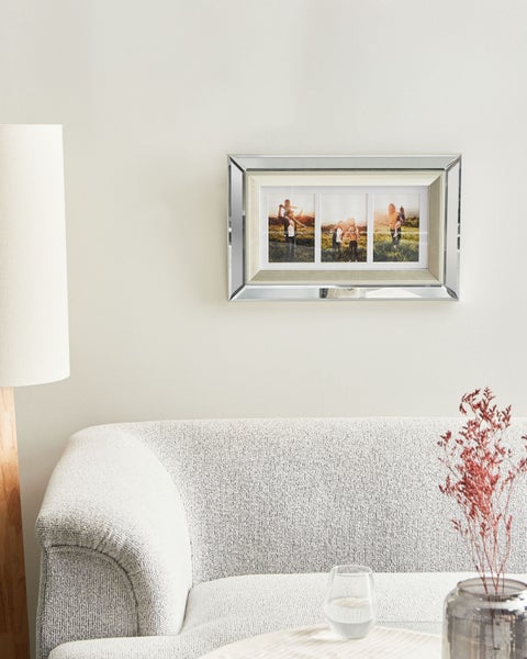 Wohnzimmer mit Sofa, Tisch, Lampe und einem silberfarbenen Fotorahmen mit drei Fotos