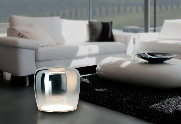 Szene mit Stehleuchte, Sofa, Tisch und Teppich in einem hellen Wohnzimmer.
