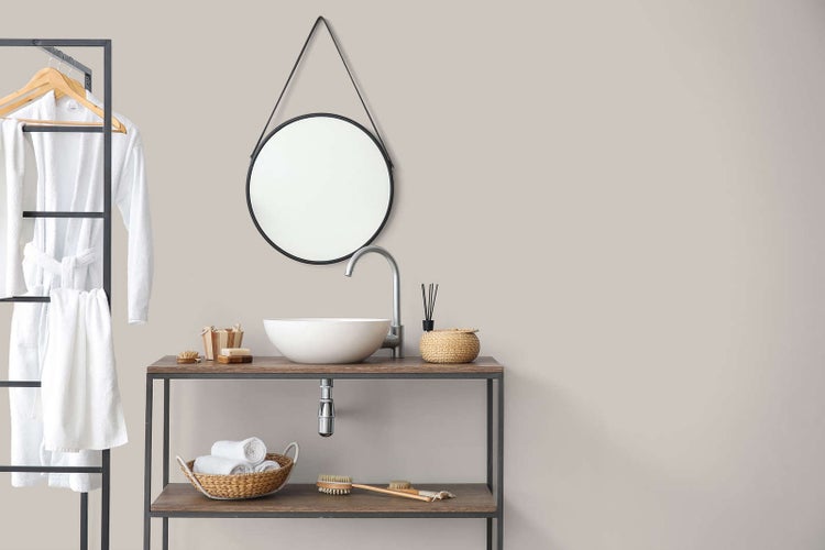 Modernes Badezimmer mit rundem Spiegel, weißem Aufsatzwaschbecken auf Holzwaschtisch und schwarzem Handtuchhalter mit Bademantel und Handtüchern.