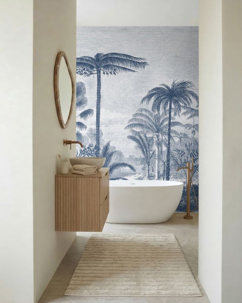 Helles Badezimmer mit blauer Palmen-Fototapete, freistehender Badewanne und Waschtisch aus Holz.