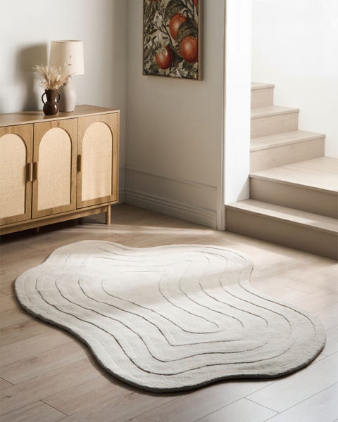 Hellbeiger, wellenförmiger Teppich mit Muster auf Holzboden in einem hellen Raum mit Sideboard und Treppe.