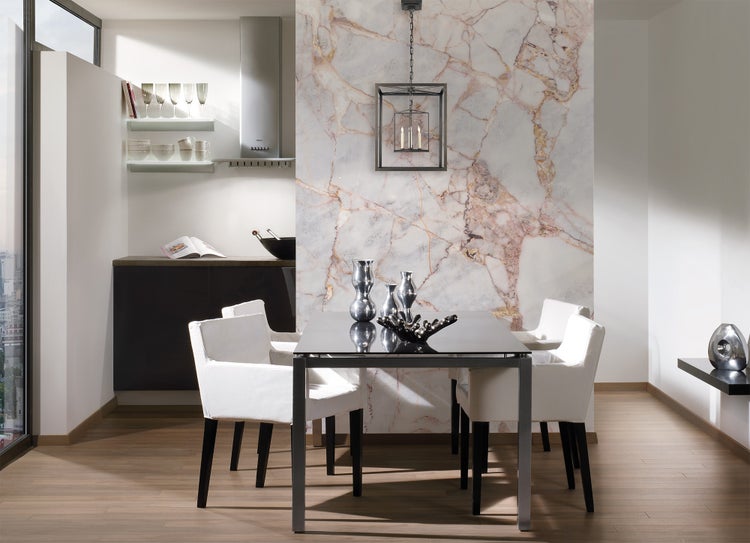 Modernes Esszimmer mit Akzentwand in Marmoroptik, dunklem Esstisch, vier weißen Polsterstühlen und einer Laternen-Hängeleuchte.