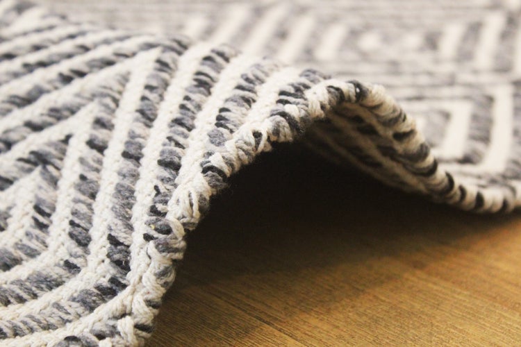 Grob gewebter Teppich mit geometrischem Muster, Detailaufnahme der Kante und Struktur.