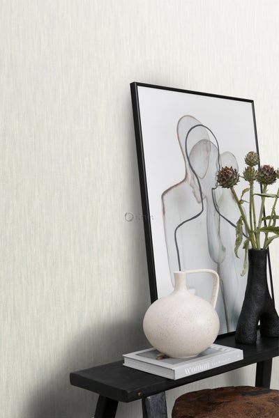 Nahaufnahme eines dekorierten Tisches mit einem gerahmten Bild, Vasen und einem Buch vor einer Wand mit Textiltapete