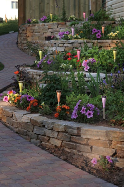 Gestufter Garten mit Steinmauer, Blumen und dekorativen Gartenleuchten