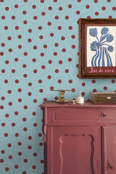 Vliestapete mit großem Punktemuster an einer Wand hinter einer roten Kommode und einem eingerahmten Bild.