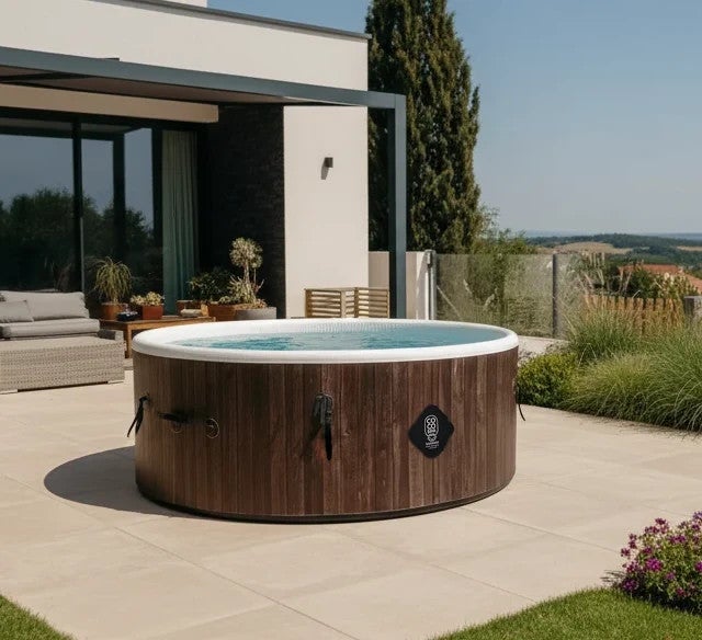 Runder aufblasbarer Whirlpool in dunkler Holzoptik auf einer modern gefliesten Terrasse in einem hellen Garten mit Haus und Loungemöbeln.