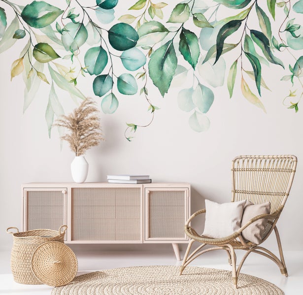 Heller Raum mit botanischer Fototapete mit Eukalyptusblättern, Rattansessel, Sideboard aus Holz mit Wiener Geflecht und Juteteppich.