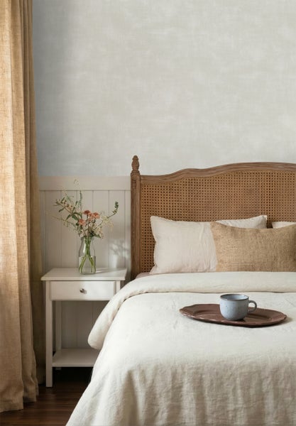Schlafzimmer mit strukturierter, cremefarbener Tapete über weißer Wandtäfelung. Holzbett mit Rattan-Kopfteil und ein weißer Nachttisch.