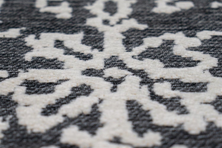 Detailansicht eines Teppichs mit flauschigem Ornamentmuster auf dunklem Webstoff.