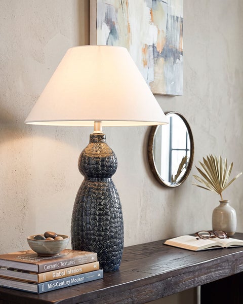 Dekorative Tischlampe mit strukturiertem Keramikfuß und klassischem Lampenschirm auf einer Anrichte in einem wohnlichen Ambiente.