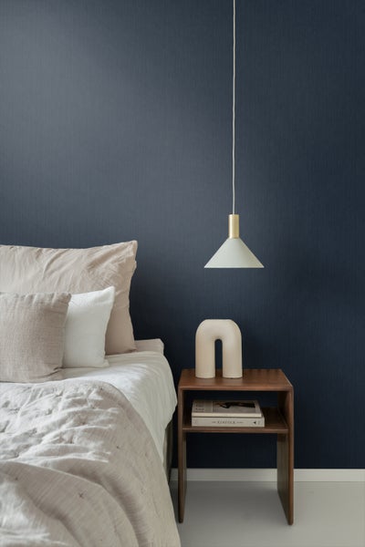 Schlafzimmer mit Bett, Nachttisch und Pendelleuchte vor einer dunklen Tapete