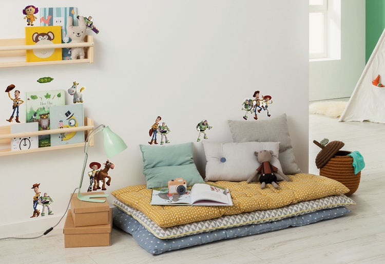 Kinderzimmergestaltung mit Wandstickern, Bücherregal, Kissen und Spielzeug für eine gemütliche Atmosphäre.