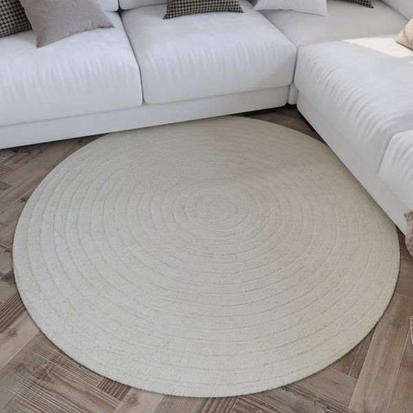 Ein runder Teppich mit Spiralmuster liegt in einem hellen Wohnzimmer vor einem Sofa auf einem Parkettboden aus Holz.