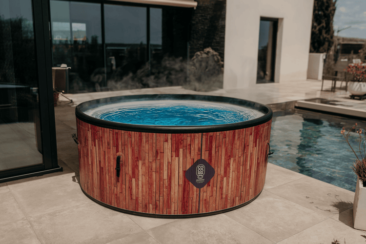 Aufblasbarer Whirlpool in Holzoptik auf einer hellen Terrasse neben einem Swimmingpool, modern gestaltet, mit Coco Spa Logo.