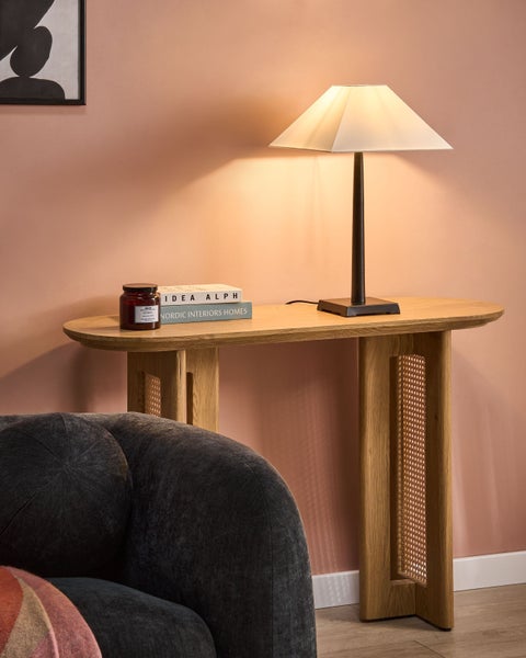 Dekoratives Interieur mit Holztisch, Lampe, Kerze, Büchern und Teil eines Sessels.