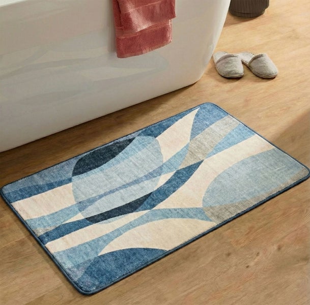 Rechteckige Badematte mit abstraktem Wellenmuster in Blau und Beige vor einer weißen Badewanne auf hellem Holzboden.