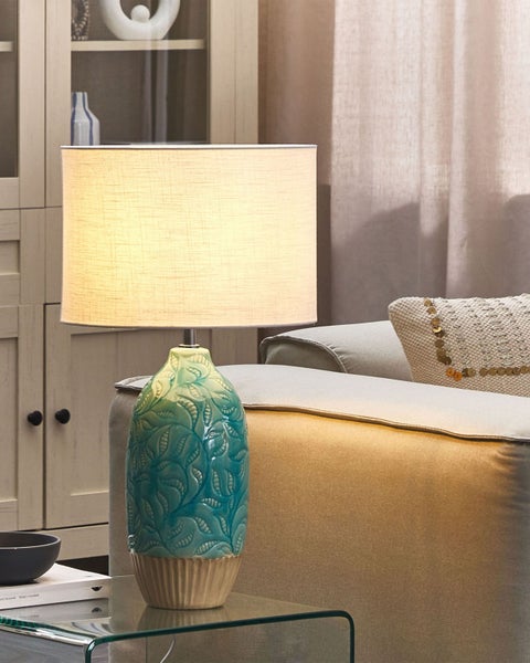 Dekorative Tischleuchte mit Stoffschirm und Keramikfuß auf einem Glastisch