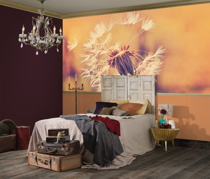 Schlafzimmer mit einer großflächigen Fototapete mit Pusteblumen-Motiv, Bett mit altem Tür-Kopfteil, Koffern und einem Kristallleuchter.